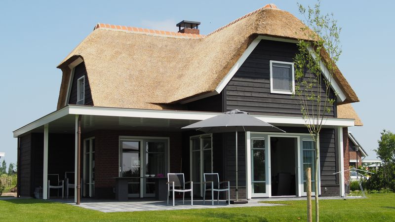 Überdachte Terrasse eines Landhauses mit Gartenmöbeln und Sonnenschirm